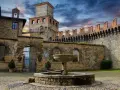 Cortile di uno dei castelli vicino Parma, con fontana in pietra e mura merlate sotto un cielo drammatico.
