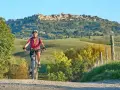 Ciclista su strada sterrata con borgo medievale sullo sfondo, un'incantevole ciclabile toscana.