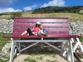 Gita domenicale con bambini nel Lazio: mamma e figlio si godono il panorama su una panchina gigante, con montagne e cielo azzurro sullo sfondo.