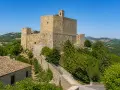 Rocche imponenti e case in pietra a Montefiore Conca, circondate da verdi colline sotto un cielo azzurro.