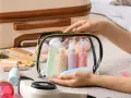 Mani che preparano cosa mettere nel beauty case: flaconi, gel e accessori da viaggio in una trousse trasparente.