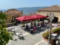 Piazza soleggiata a Castellabate con tavolini all'aperto e gente che si gode il momento. La scritta "qui non si muore" invita a rilassarsi.