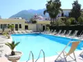 Piscina con lettini e palme, vista su montagne e chiesa. Un luogo ideale per rilassarsi, come suggeriscono le hotel terme punta del sole recensioni.