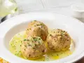 Tre canederli piatti tipici del Trentino Alto Adige, serviti in un brodo dorato e guarniti con erba cipollina.