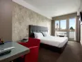 Camera moderna con letto matrimoniale, scrivania in vetro, poltrona rossa e balcone con vista. I prezzi su Booking sono a persona.