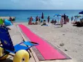Una spiaggia attrezzata per gite per disabili, con una passerella rosa e una sedia a rotelle speciale per la sabbia.