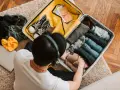 Preparazione per la gita: valigia aperta con vestiti piegati, scarpe, cintura, cappello giallo e laptop.