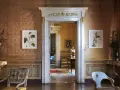 Interni della Casina Vanvitelliana: un salone con tappezzeria damascata, quadri botanici, mobili d'epoca e un'apertura su un'altra stanza.