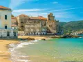 Spiaggia dorata e mare cristallino a Castellabate, con antichi palazzi e un castello che si affacciano sull'acqua. Un posto al mare da sogno.