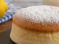 Torta al vento mantovana soffice e leggera, cosparsa di zucchero a velo. Accanto, un limone e un tovagliolo a righe blu.