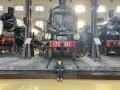 Bambino seduto davanti a un imponente treno storico al Museo di Pietrarsa, Napoli.