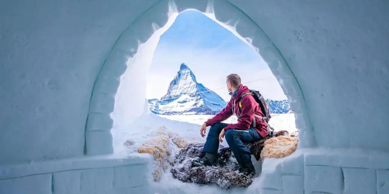 Un uomo ammira il maestoso Cervino dall'interno di un igloo, un'esperienza unica di dormire in un igloo in Italia.