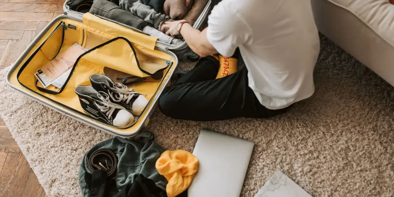 Preparazione per il viaggio: cosa si può portare in aereo. Valigia aperta con scarpe, vestiti, laptop e mappa.
