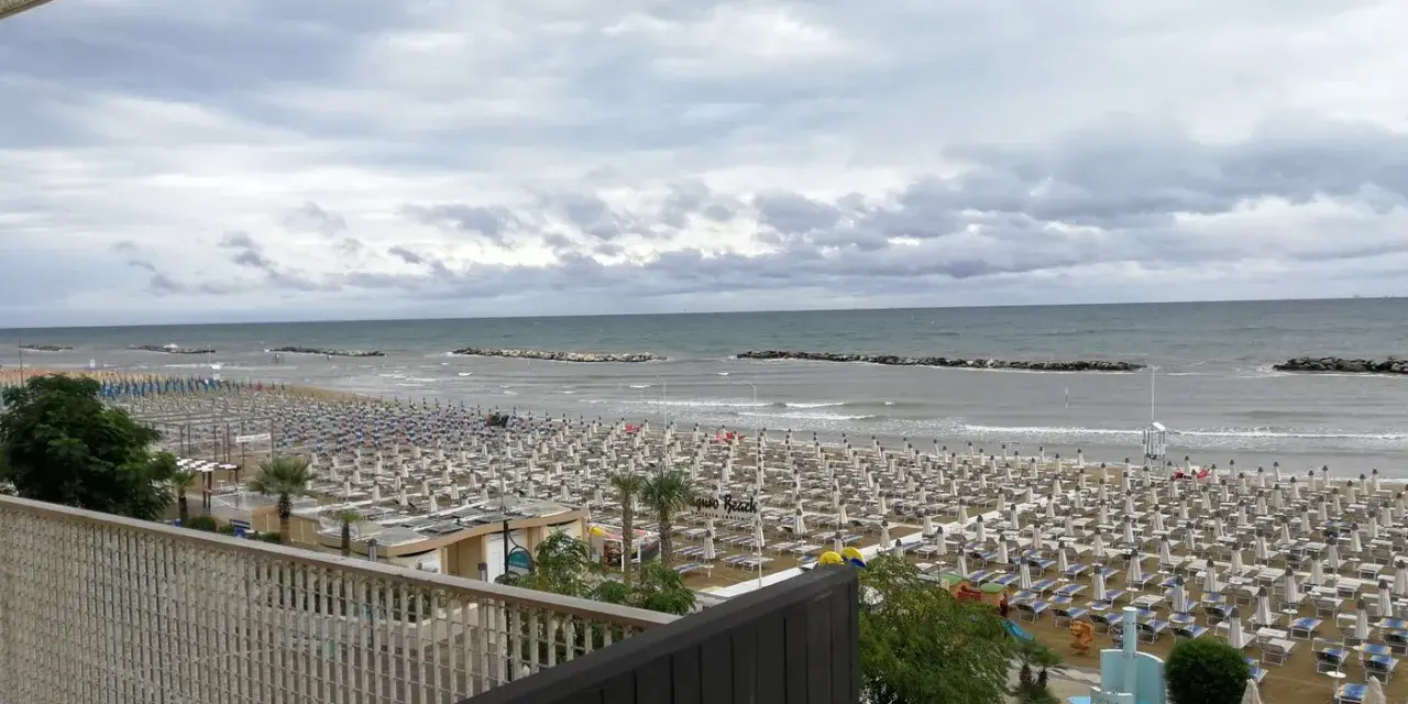 Spiaggia affollata di lettini e ombrelloni, con il mare calmo e il cielo nuvoloso. Vista dal piccadilly hotel bellaria.