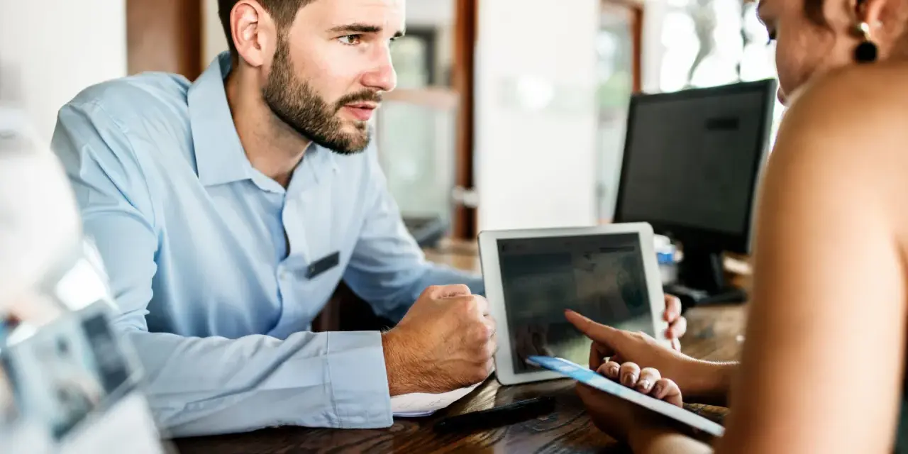 Receptionist con tablet mostra a cliente che non ci sono più camere, un caso di overbooking hotel.