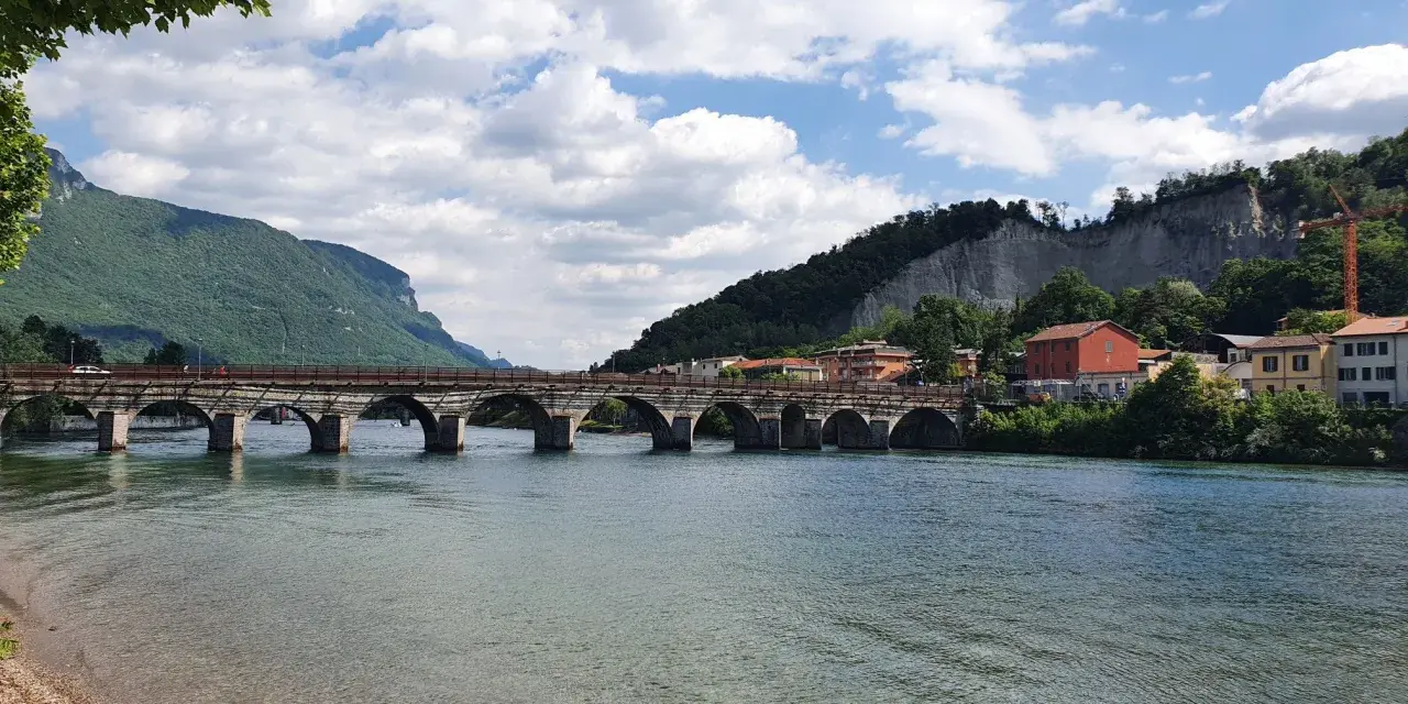 Ponte storico sul fiume Adda, con montagne verdi e case colorate. Un'ottima vista per scoprire cosa vedere a Calolziocorte.