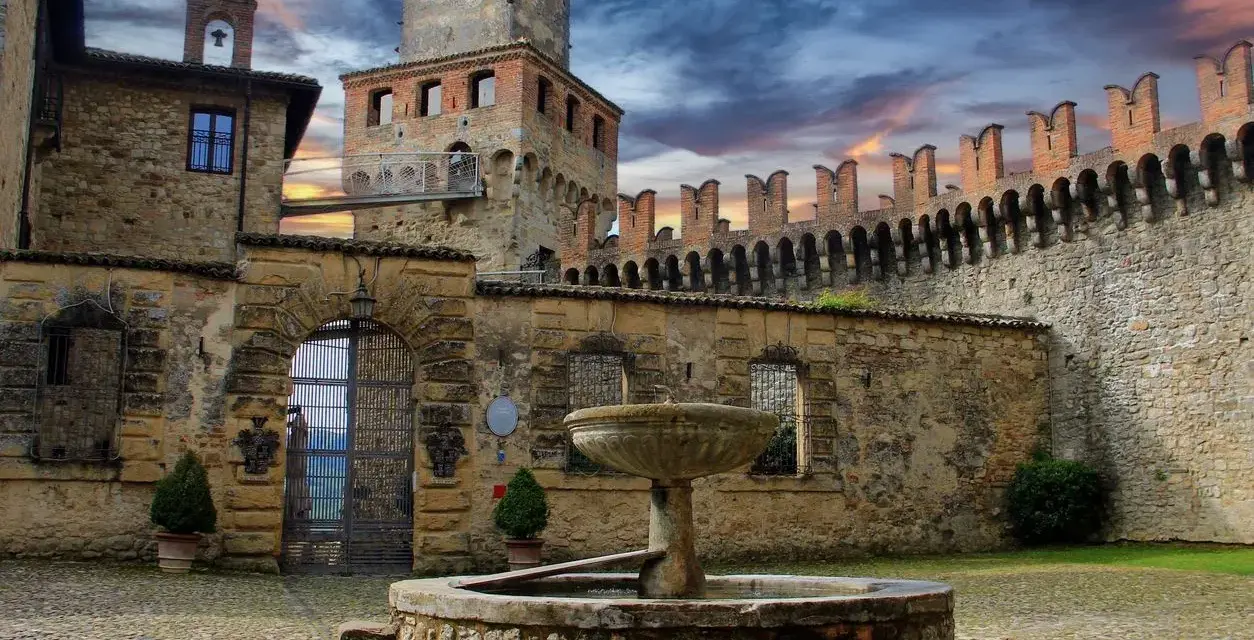 Cortile di uno dei castelli vicino Parma, con fontana in pietra e mura merlate sotto un cielo drammatico.