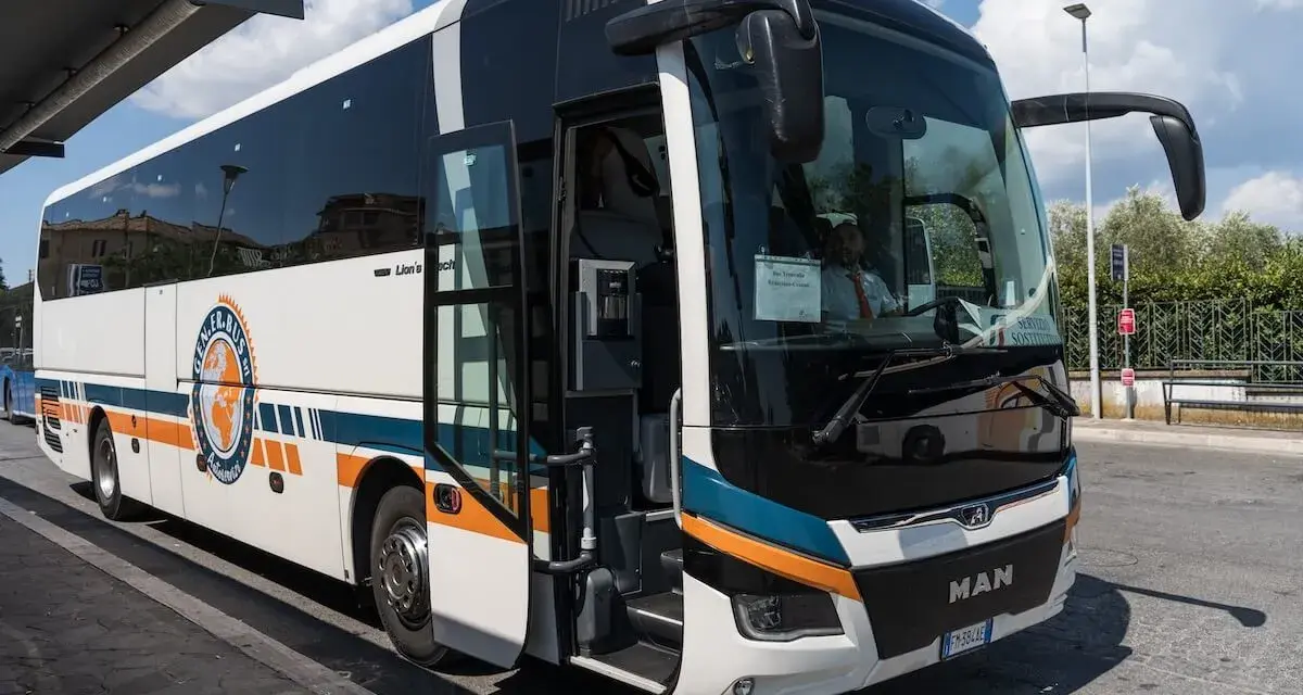 Autobus FlixBus pronto a partire da Agropoli per Roma. Il mezzo bianco con strisce arancioni e blu attende i passeggeri sotto un cielo azzurro.