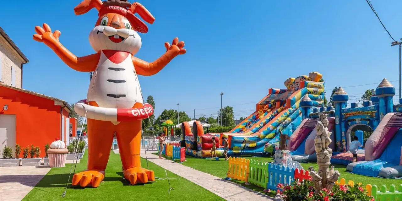 Gigante coniglio gonfiabile "Ciccio" accoglie i bambini in un parco giochi con scivoli e castelli gonfiabili, un'oasi di divertimento per gli ospiti dell'hotel Ciccio.