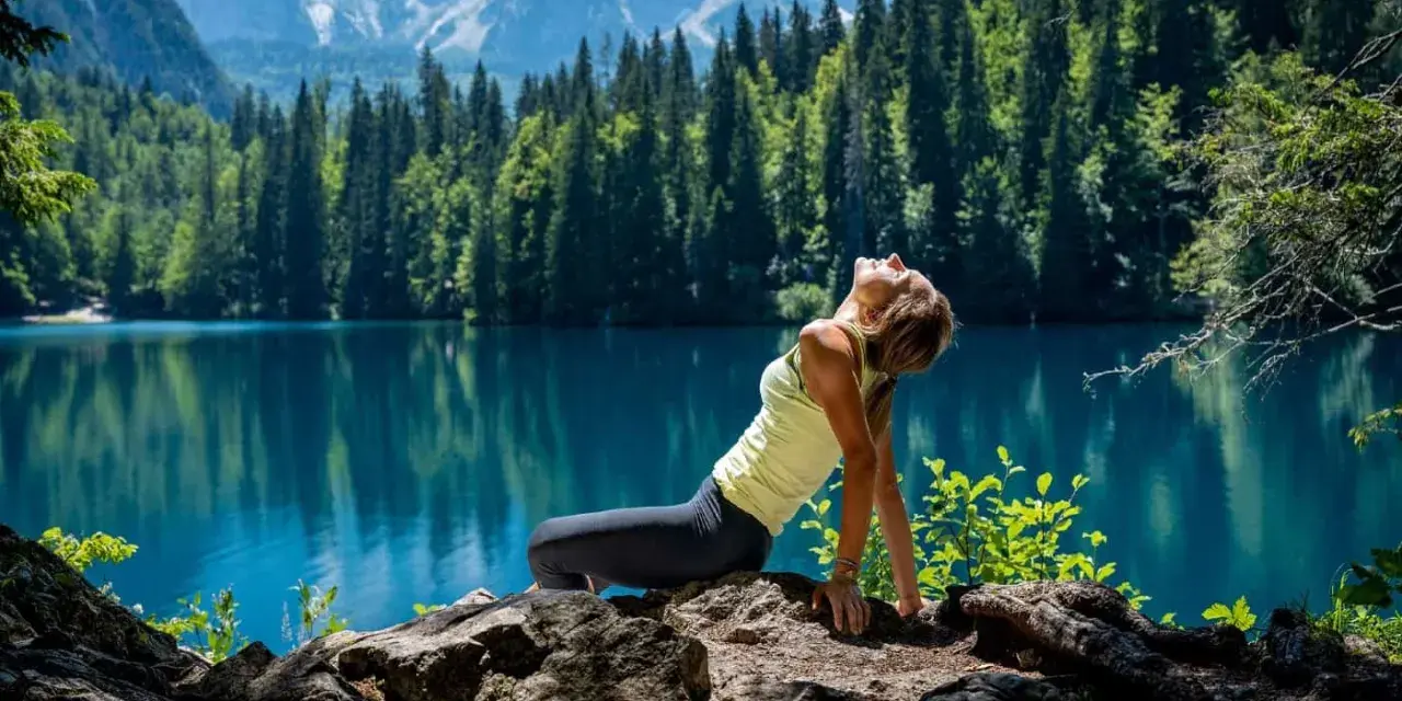 Donna in posa yoga su rocce, con lago turchese e montagne sullo sfondo. Un'immagine di serenità nella friuli montagna estate.