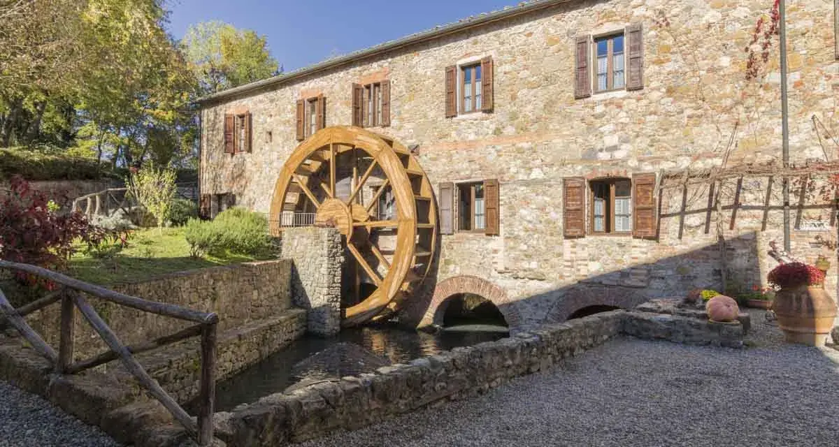 Mulino in pietra con ruota in legno, perfetto per le gite da Tuscany. Un angolo di pace tra alberi e acqua.