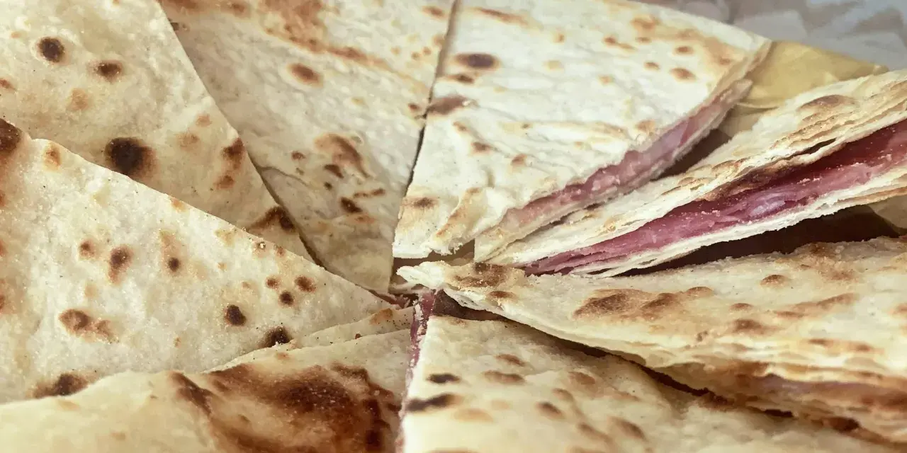 Piadina sfogliata ricetta originale, con strati sottili e ripieno di salumi, pronta per essere gustata.