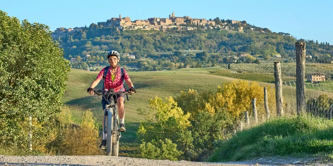 Ciclista su strada sterrata con borgo medievale sullo sfondo, un'incantevole ciclabile toscana.