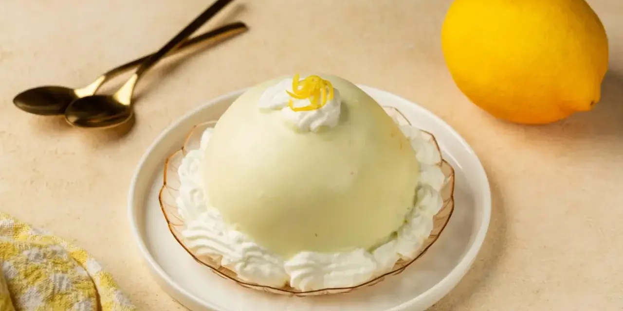 Dolce al limone, perfetto per scoprire cosa mangiare a Salerno. Servito con panna e scorzetta, pronto per essere gustato con cucchiaini dorati.