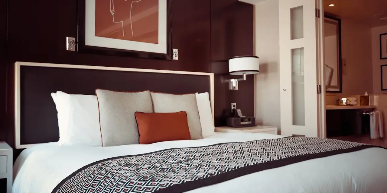 Letto in una camera doppia, con copriletto geometrico e quadro astratto. Il significato di camera doppia è un luogo accogliente.