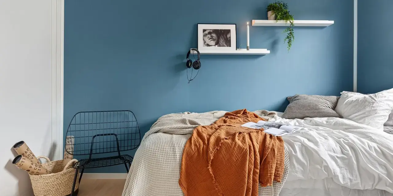 Camera da letto moderna con letto, coperta arancione, cestino e sedia in metallo. Utile per la classificazione camere hotel.