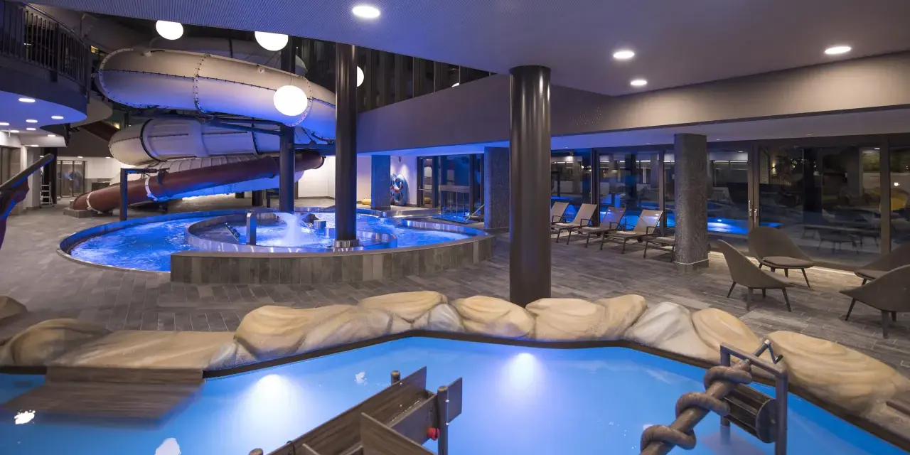 Piscina interna con scivoli acquatici e giochi d'acqua al Quellenhof Merano, un'oasi di divertimento e relax.