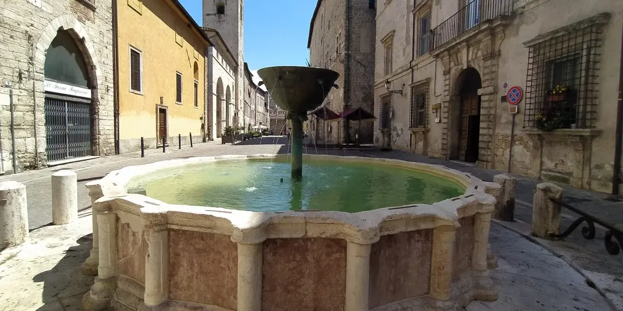 Fontana storica in pietra, un luogo incantevole tra le cose da vedere a Narni, con edifici antichi e un campanile sullo sfondo.