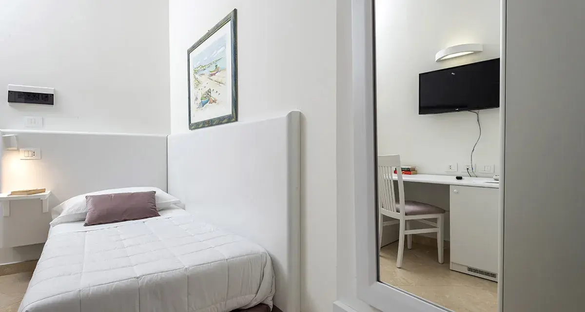 Accogliente camera singola hotel con letto, scrivania e TV visibili nello specchio.