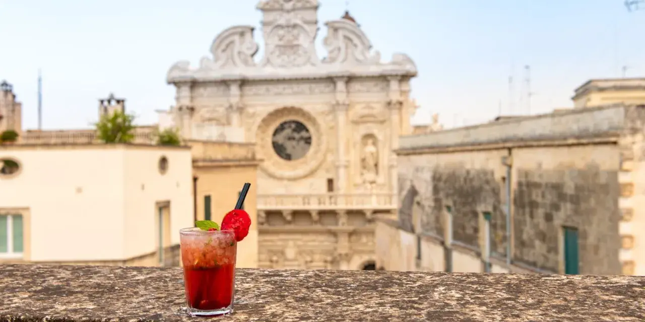 Cocktail rosso con fragola e menta, sullo sfondo la Basilica di Santa Croce. Il miglior aperitivo a Lecce.