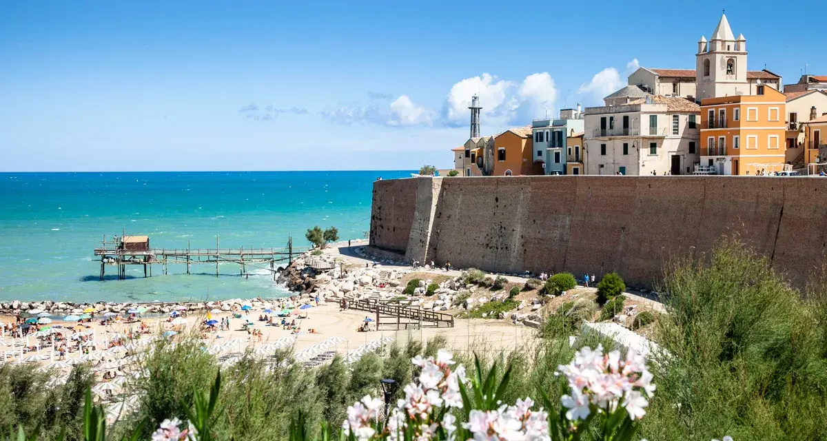 Vista di una spiaggia affollata con un trabucco sul mare e il borgo antico di Termoli. Perfetto per scoprire cosa vedere vicino a Termoli.