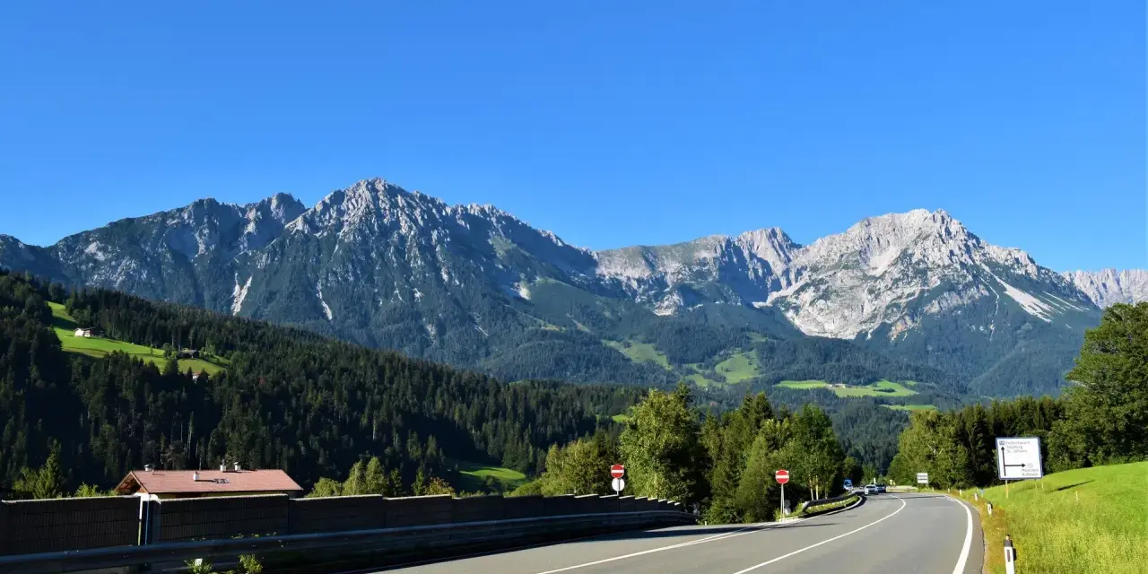 Strada panoramica per viaggi in auto in Europa dall'Italia, con montagne imponenti e boschi verdi.