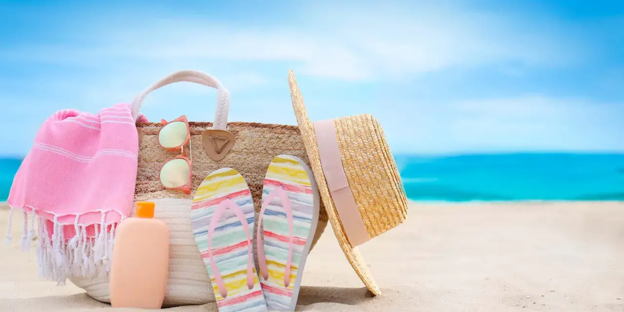 Borsa da spiaggia con asciugamano rosa, infradito colorate, occhiali da sole e cappello di paglia. Ecco cosa portare al mare per una giornata perfetta!