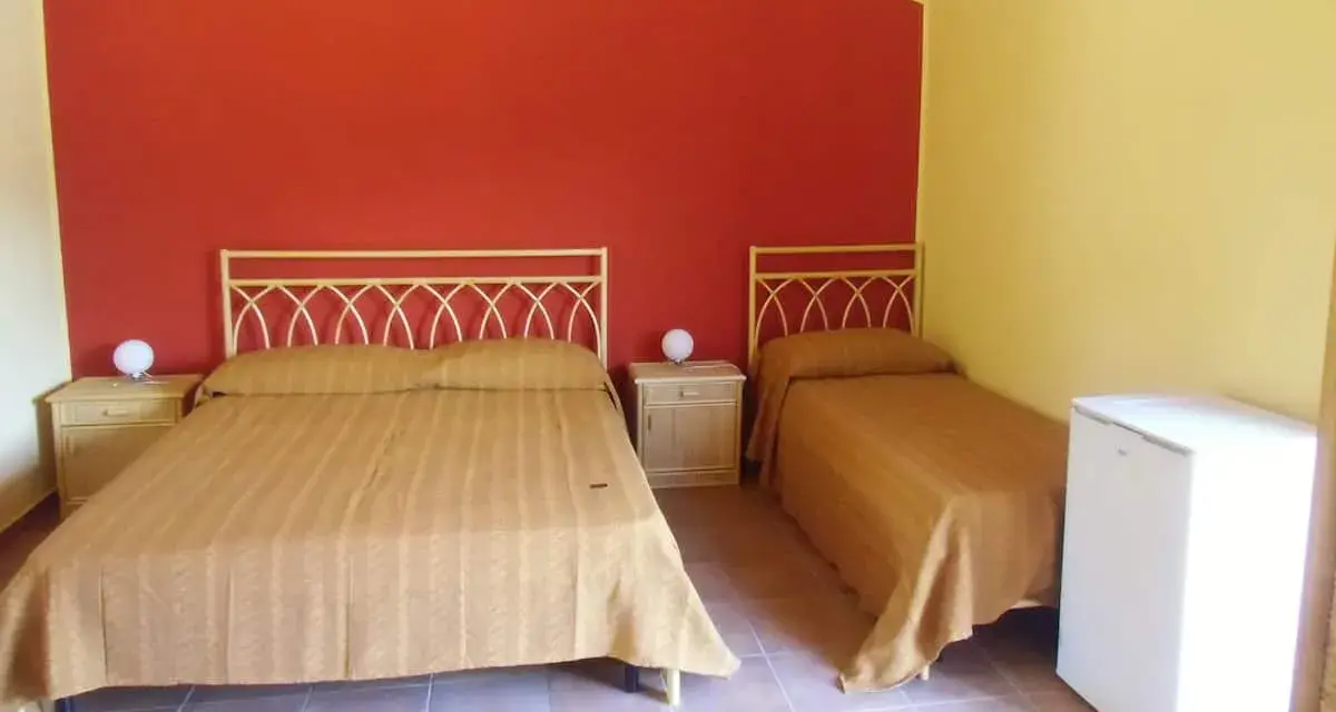 Camera semplice in un albergo una stella: due letti singoli e un letto matrimoniale con copriletti color ocra, pareti rosse e gialle, comodini e un piccolo frigorifero.