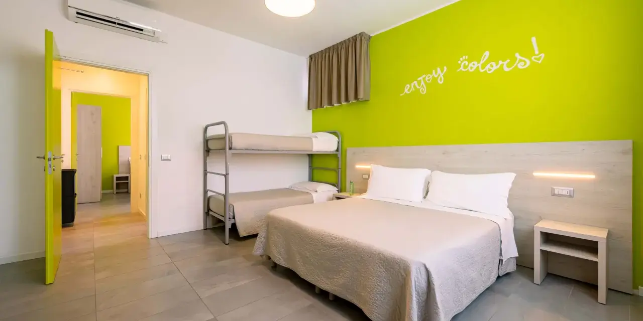 Camera luminosa con letto matrimoniale, letto a castello e parete verde brillante. Un invito a godersi i colori del green village Cesenatico.