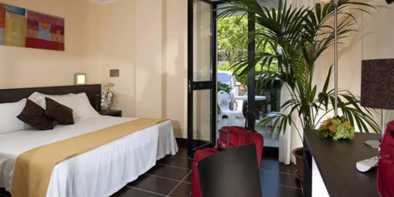 Camera accogliente al Park Hotel Kursaal Misano, con letto comodo, piante verdi e valigie rosse pronte per la partenza.