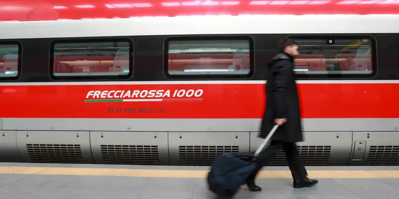 Uomo con bagagli ingombranti cammina lungo il Frecciarossa 1000.