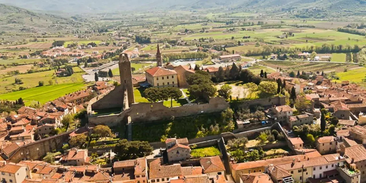 Un borgo medievale in collina, perfetto per un tour Toscana 4 giorni. Case con tetti rossi e una torre imponente dominano il paesaggio verdeggiante.