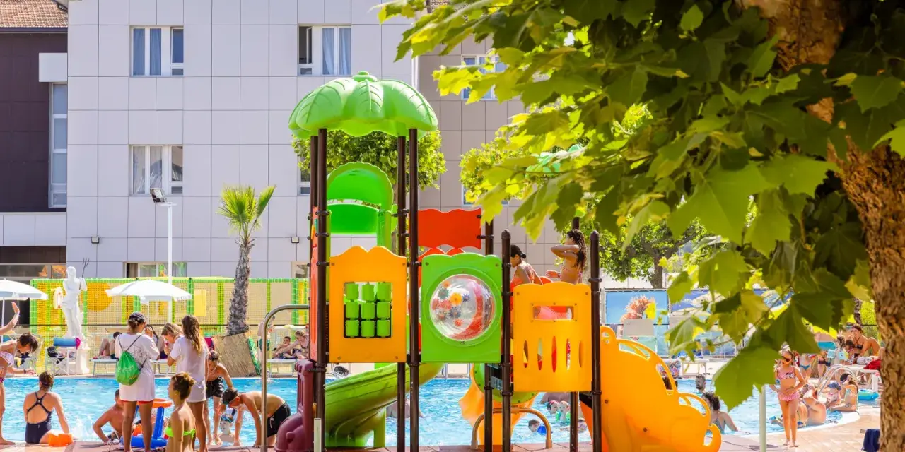 Bambini giocano in piscina e su uno scivolo colorato, un'immagine che riflette le positive recensioni di Color Perla Village.