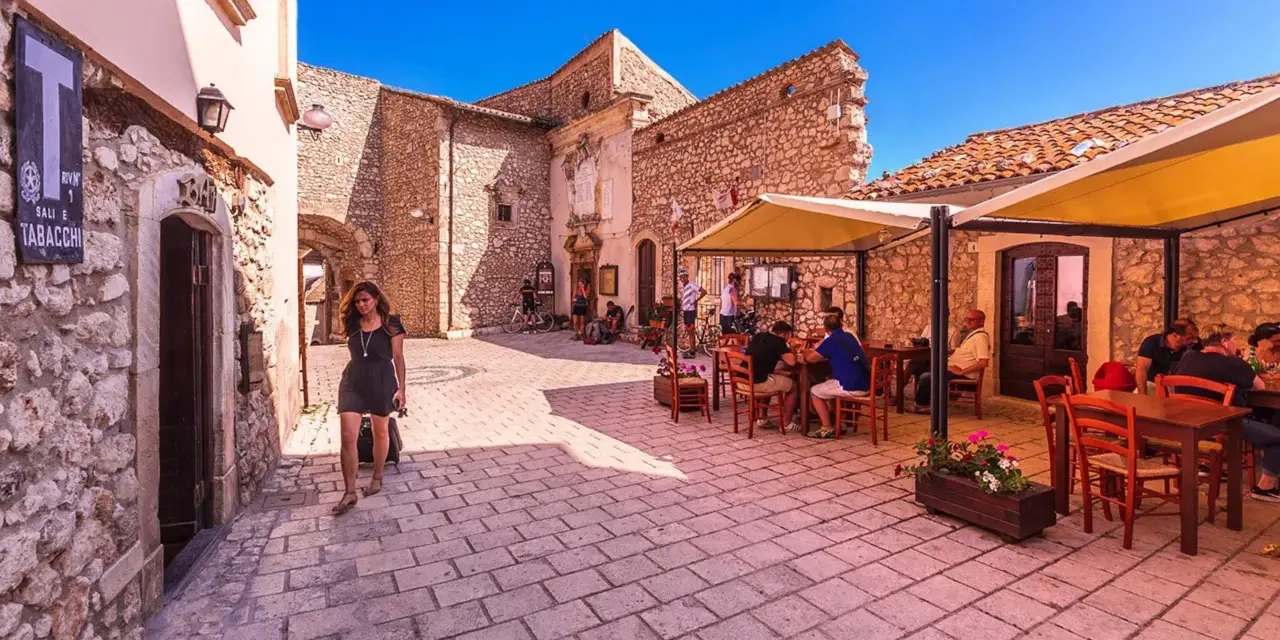 Una donna cammina in un vicolo di Santo Stefano di Sessanio, dove si trovano i migliori ristoranti. Tavoli all'aperto invitano a gustare la cucina locale.