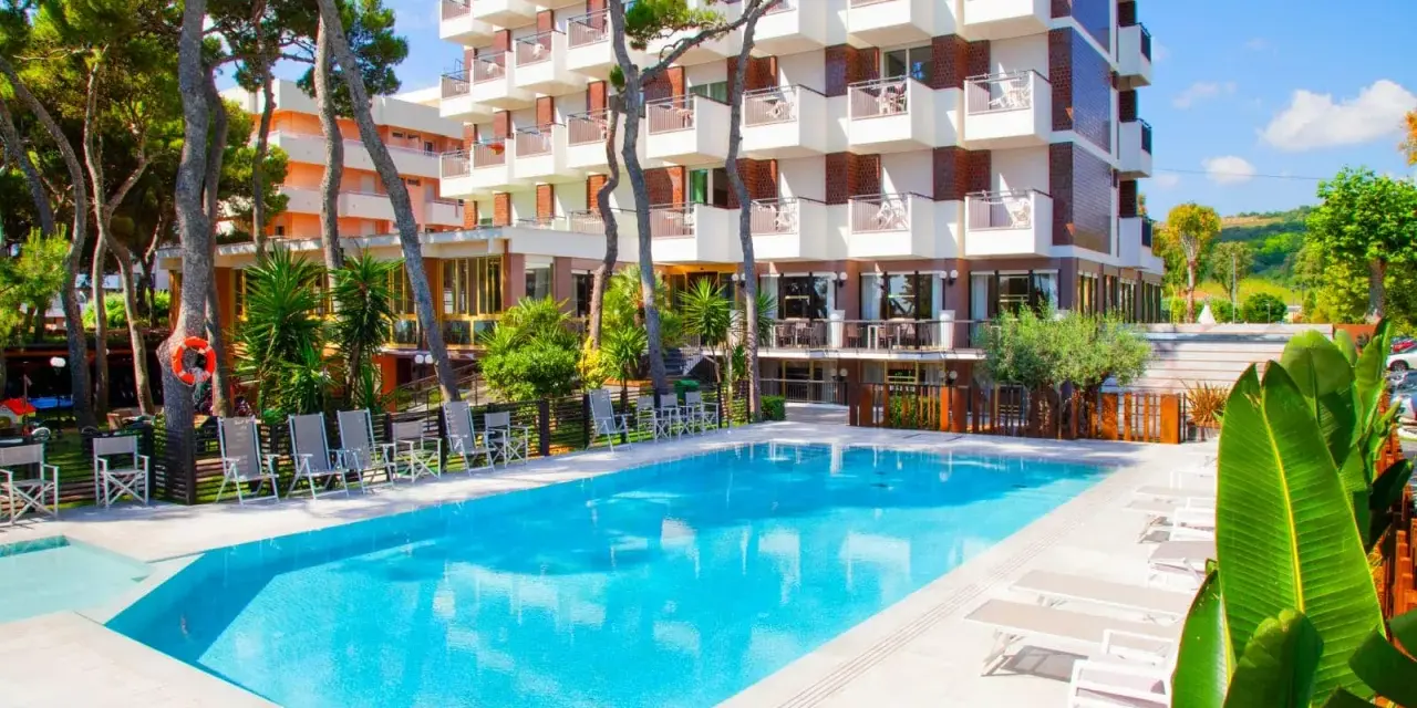 Piscina azzurra e lettini prendisole davanti al **promenade hotel giulianova**, circondati da pini e vegetazione lussureggiante.