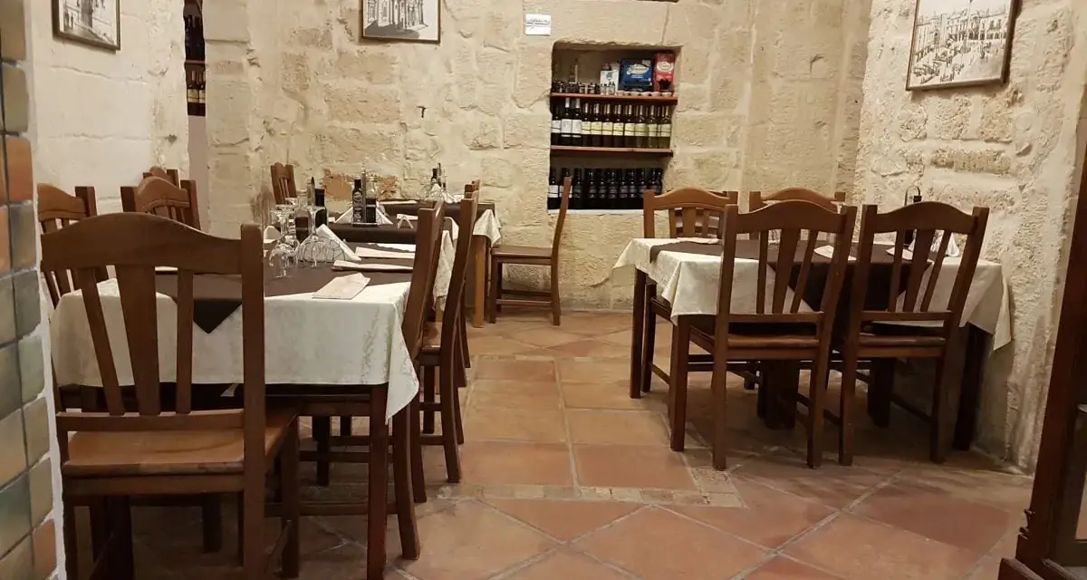 Atmosfera intima per scoprire dove cenare a Lecce: tavoli apparecchiati in pietra leccese, bottiglie di vino e quadri d'epoca.