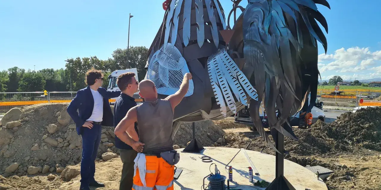 Operai al lavoro su un imponente gallo romagnolo in metallo, un'opera d'arte che domina il paesaggio.