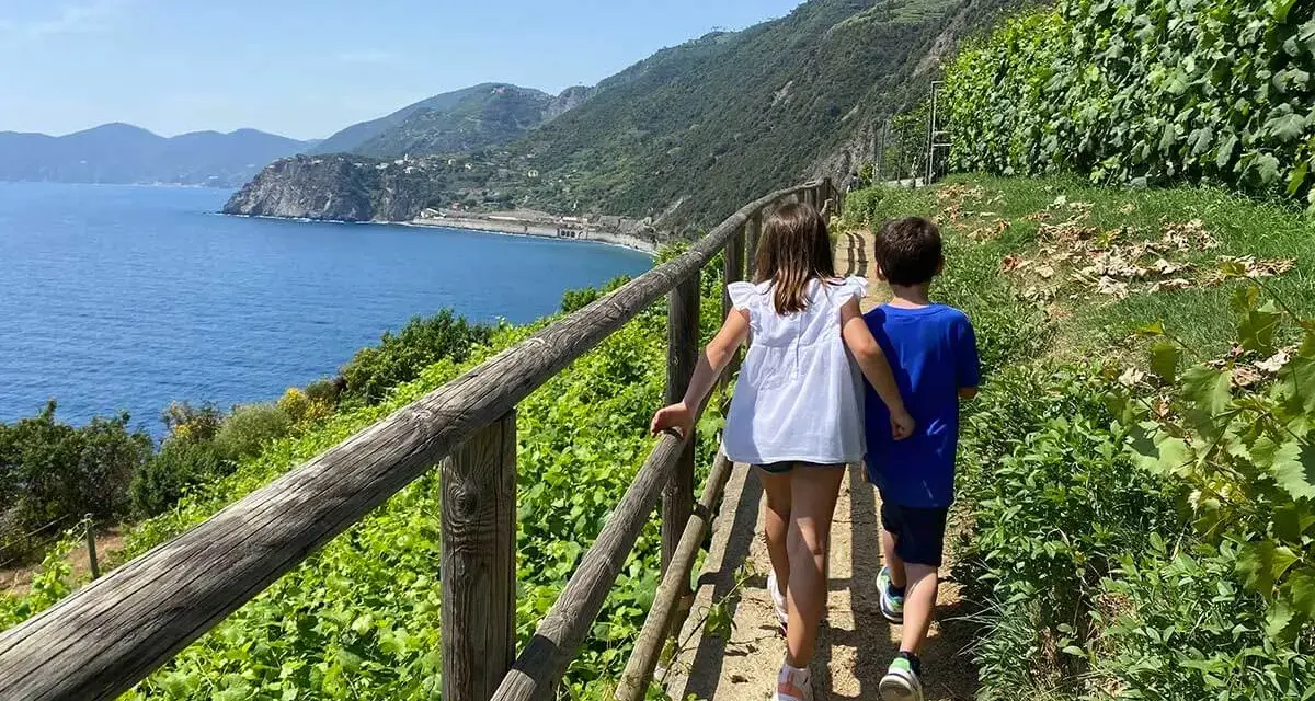 Bambini esplorano i sentieri panoramici delle Cinque Terre, con il mare blu e la vegetazione rigogliosa.