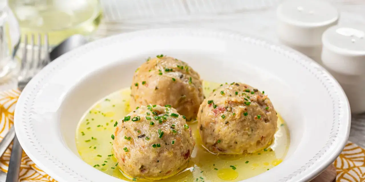 Tre canederli piatti tipici del Trentino Alto Adige, serviti in un brodo dorato e guarniti con erba cipollina.