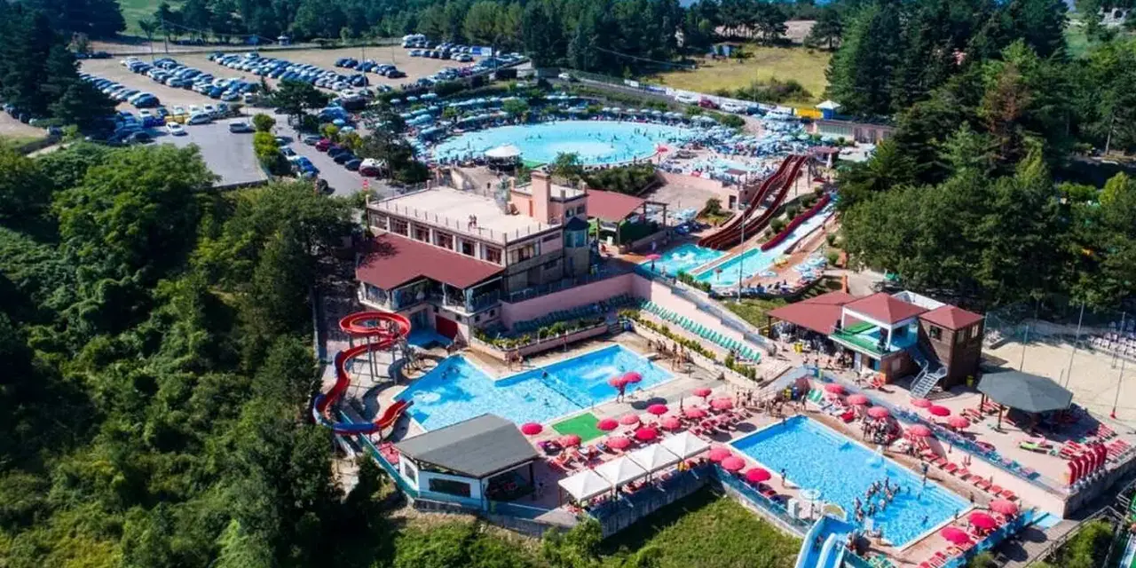 Un grande parco acquatico nelle Marche, con scivoli, piscine e tante persone che si divertono sotto il sole.